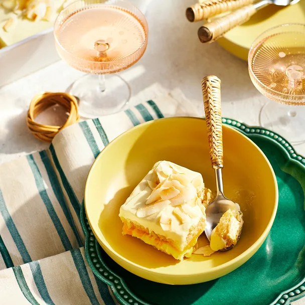 A slice of limoncello tiramisu with passionfruit curd in a yellow bowl with a spoon.