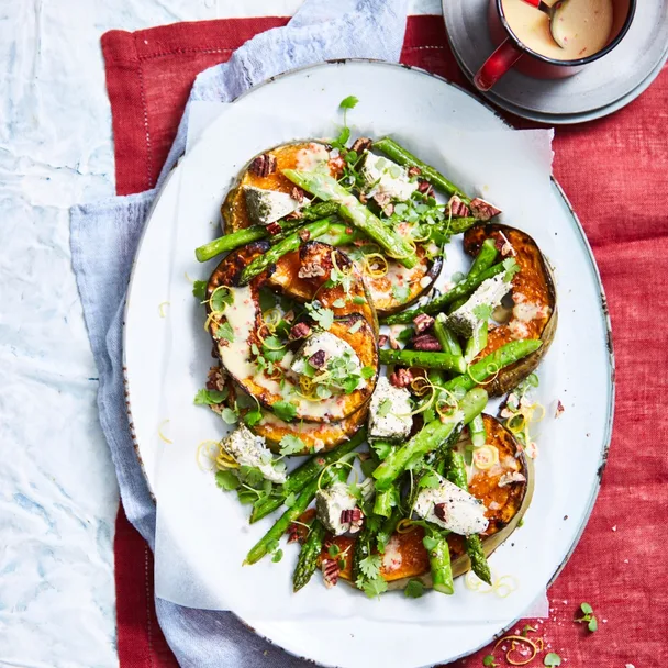 Roasted pumpkin & asparagus on a white platter over a red cloth, and a cup of buttermilk dressing.