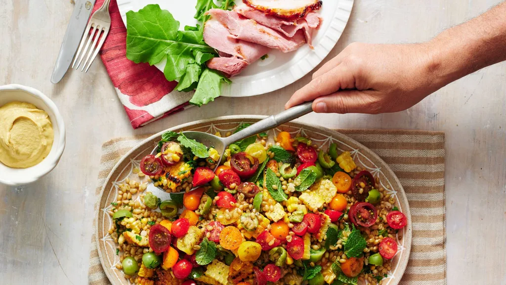 Grain salad on a platter next to a platter of ham sliced