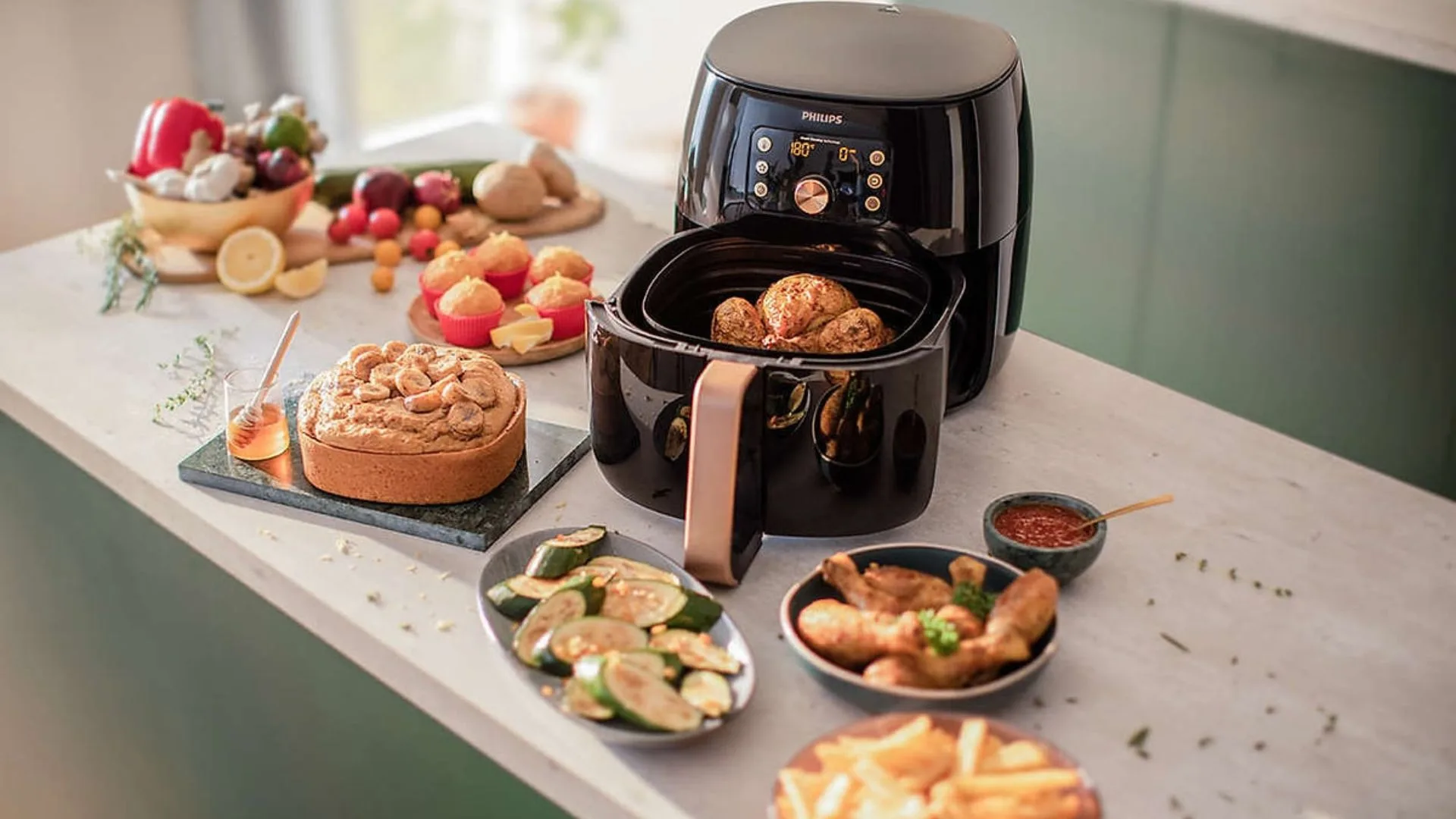 Kitchen scene showing a Philips air fryer cooking a chicken, with various prepared foods on the counter.