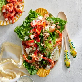 cold prawn salad with creamy lemon dressing on an oval platter with salad servers and a tea towel.