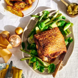 Pork shoulder roast on a platter with green vegetables.
