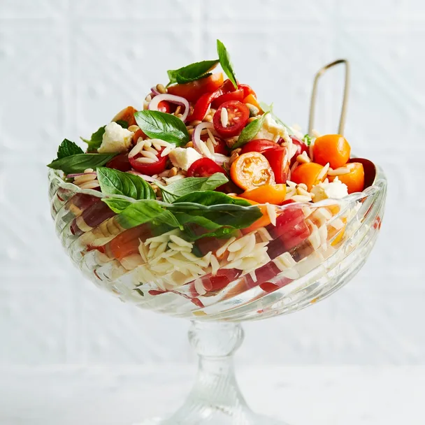 orzo salad recipe in a glass serving dish on a white bench