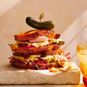 Toasted ham and cheese sandwich with a pickle on top, sitting on a stone slab.