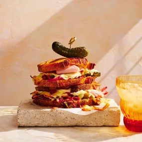 Toasted ham and cheese sandwich with a pickle on top, sitting on a stone slab.