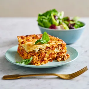 slice of chicken mushroom lasagne on a blue plate with salad in background