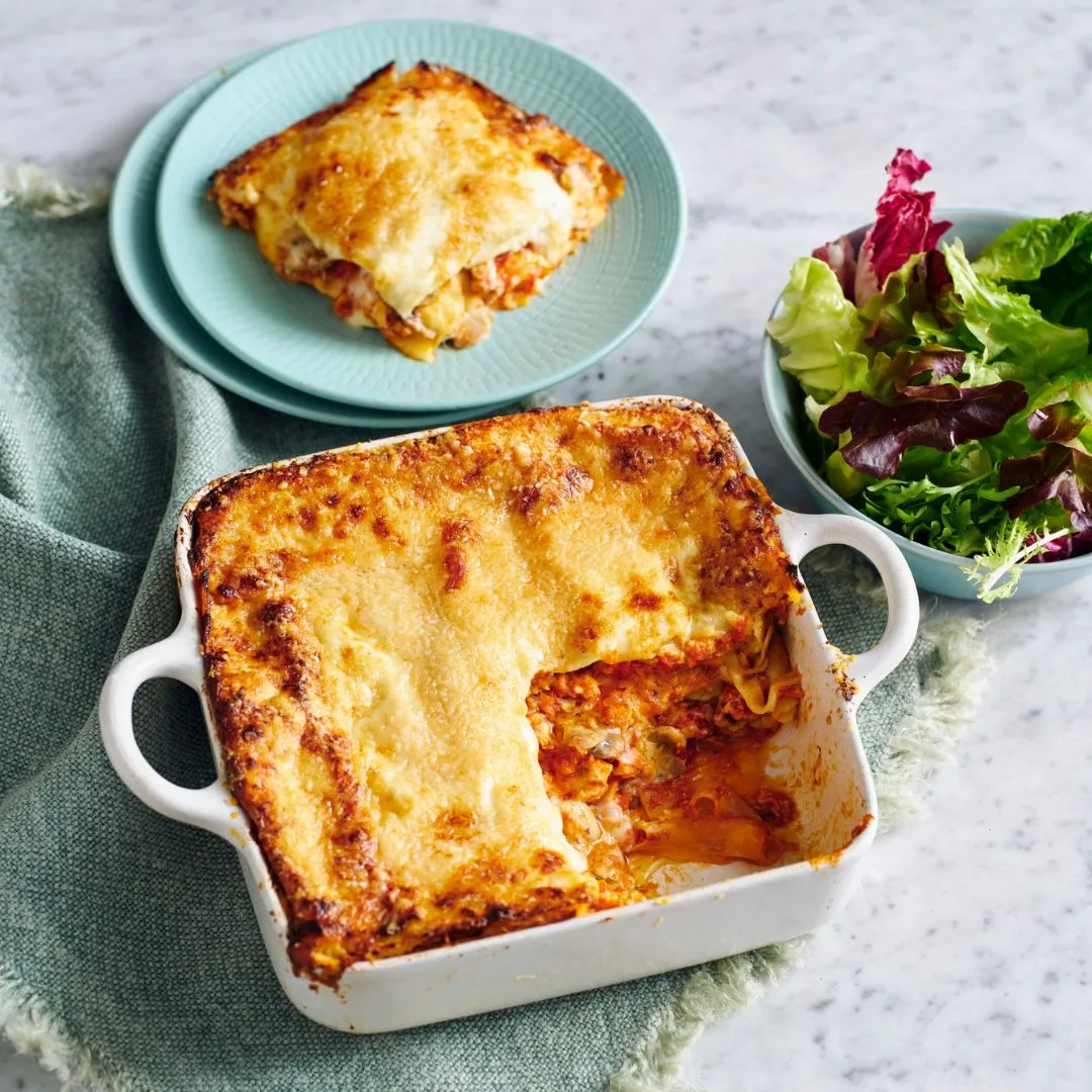 chicken mushroom lasagne in a white baking dish with one slice removed