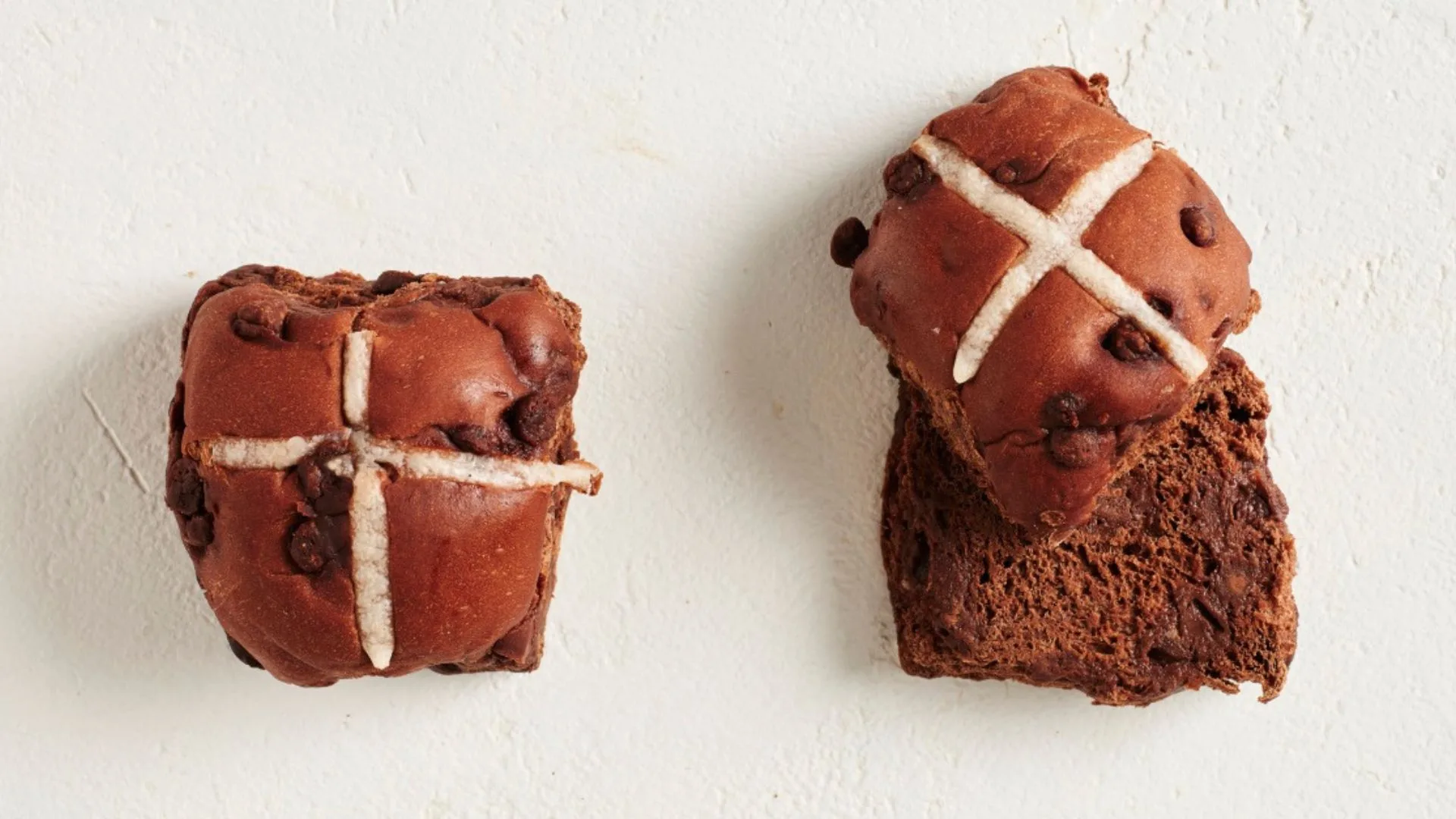 two chocolate hot cross buns, one cut in half