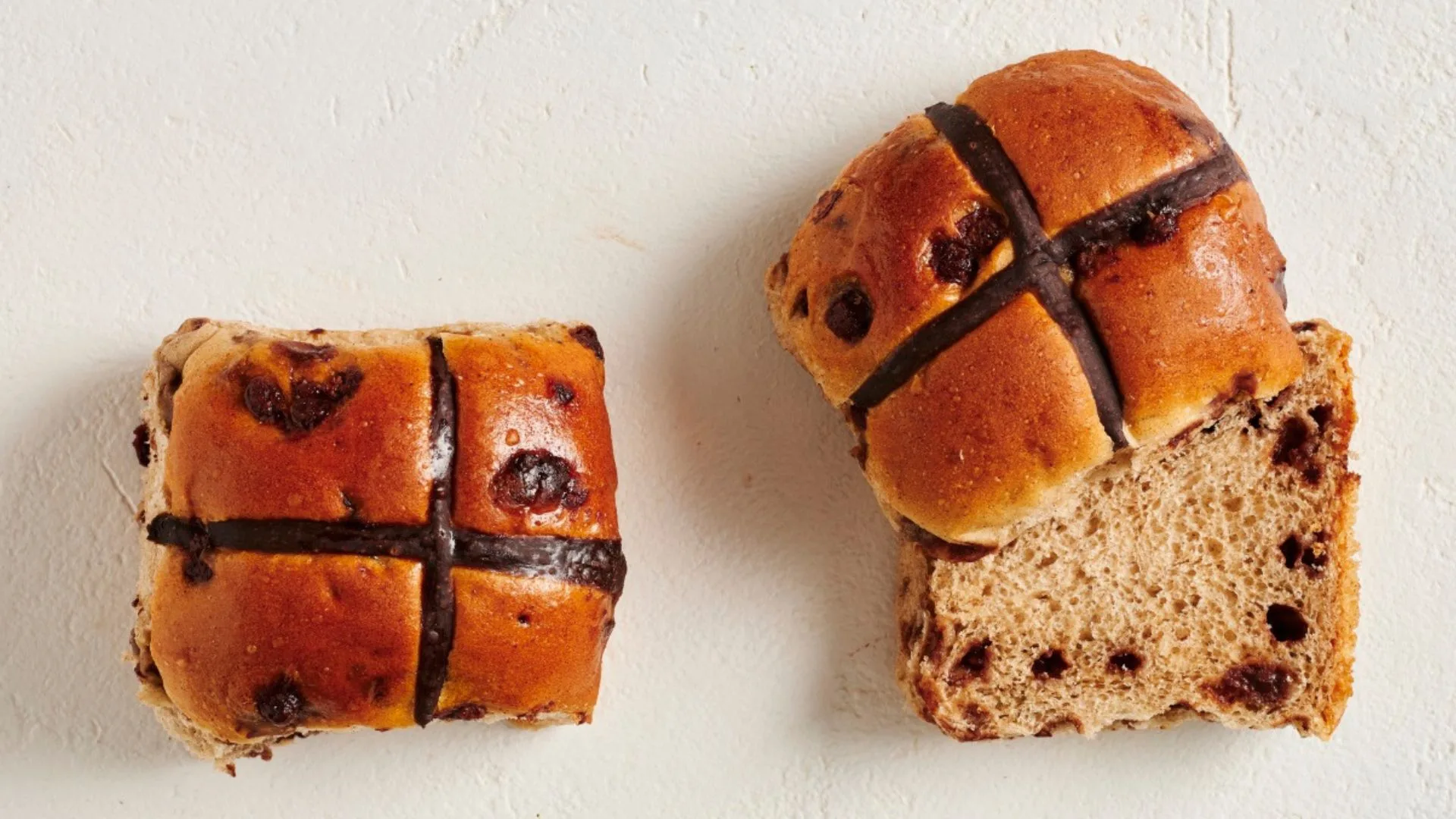 two chocolate hot cross buns, one cut in half