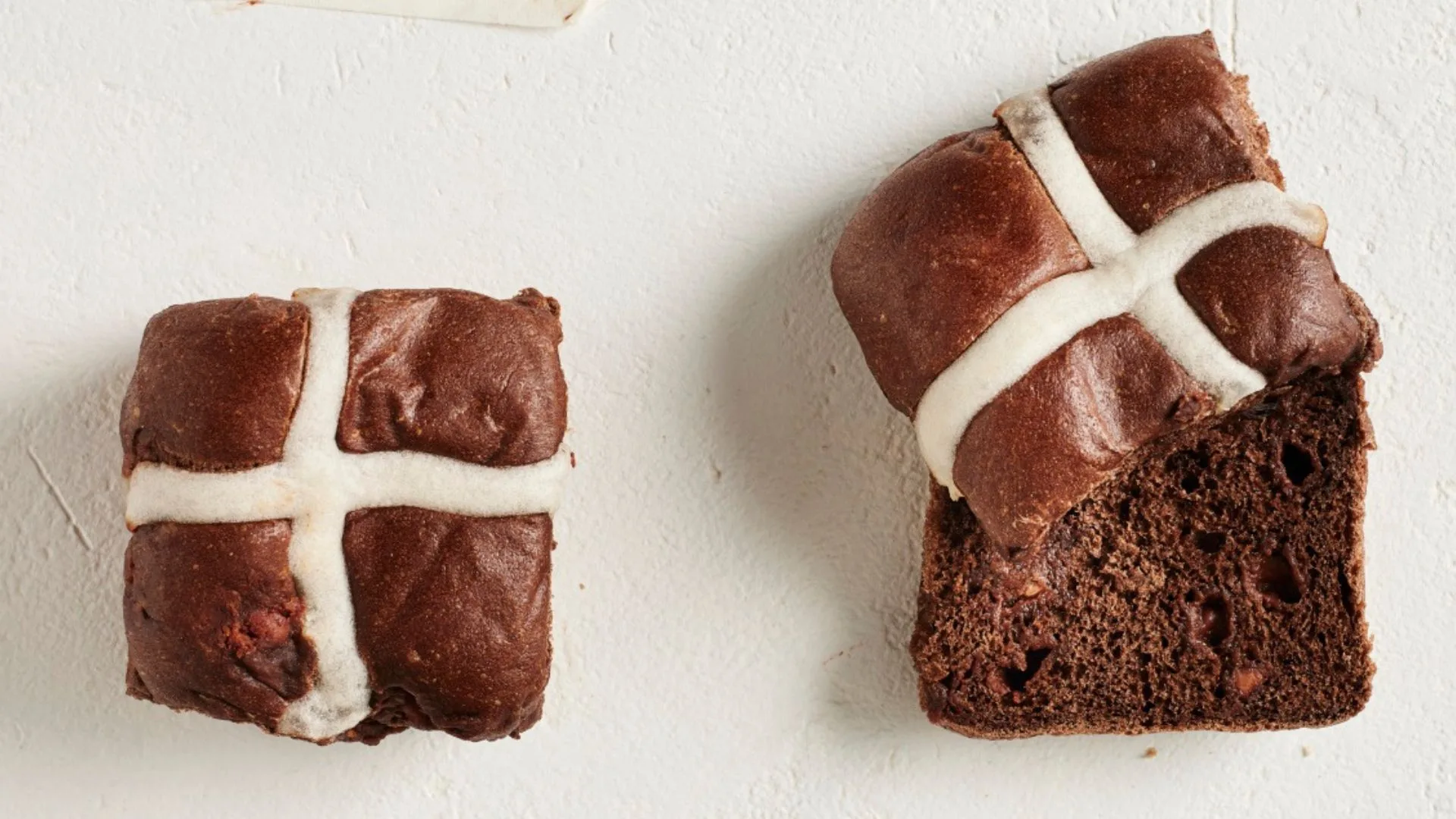 two chocolate hot cross buns, one cut in half