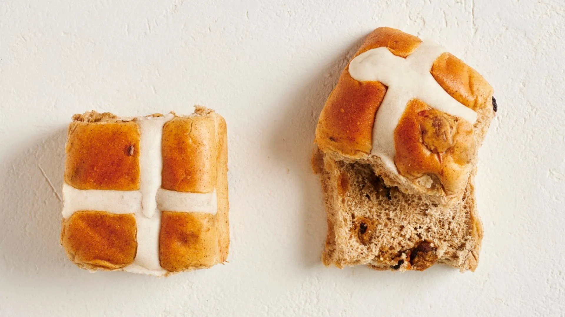 two tradition hot cross buns, one cut in half