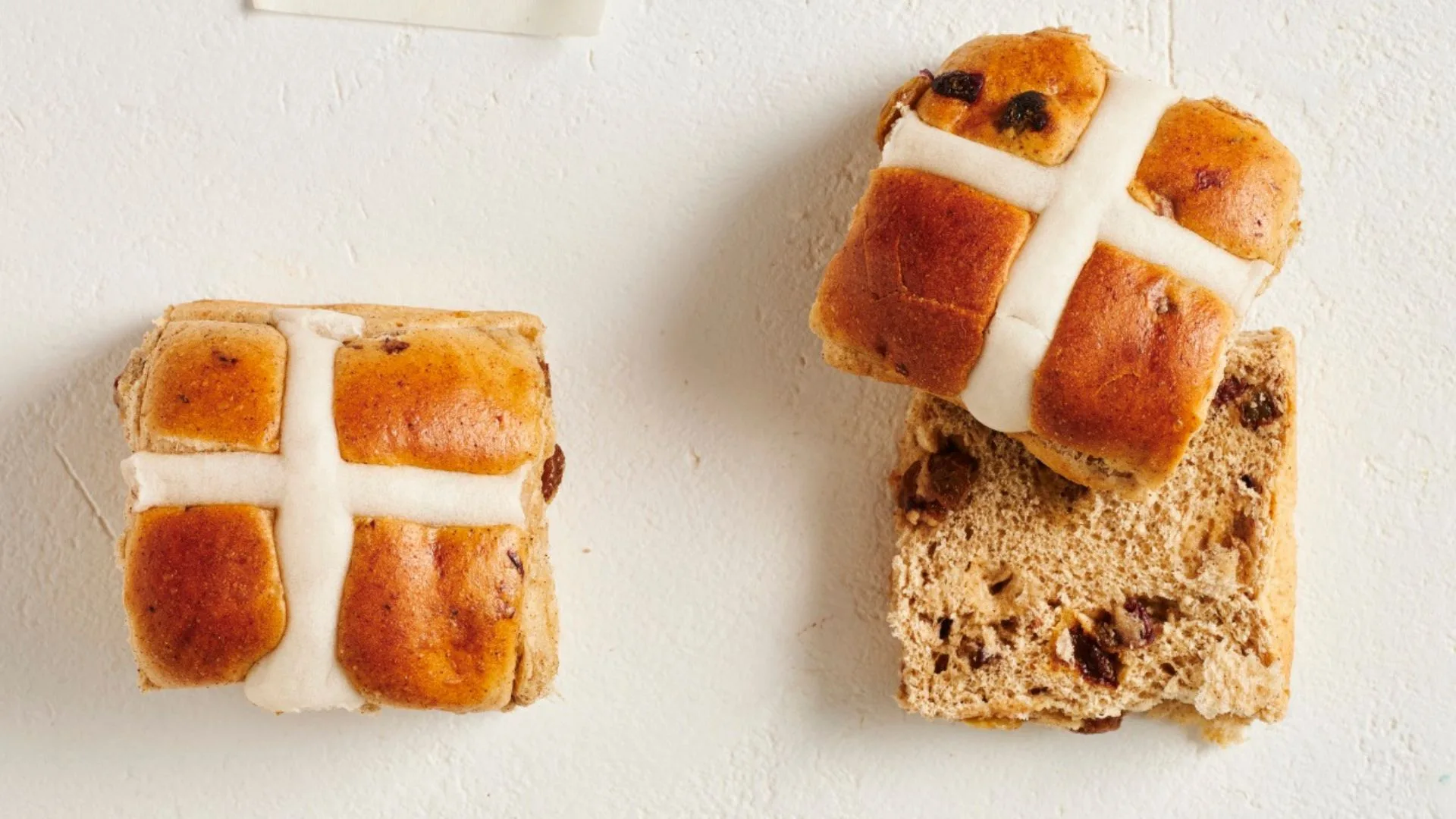 two tradition hot cross buns, one cut in half