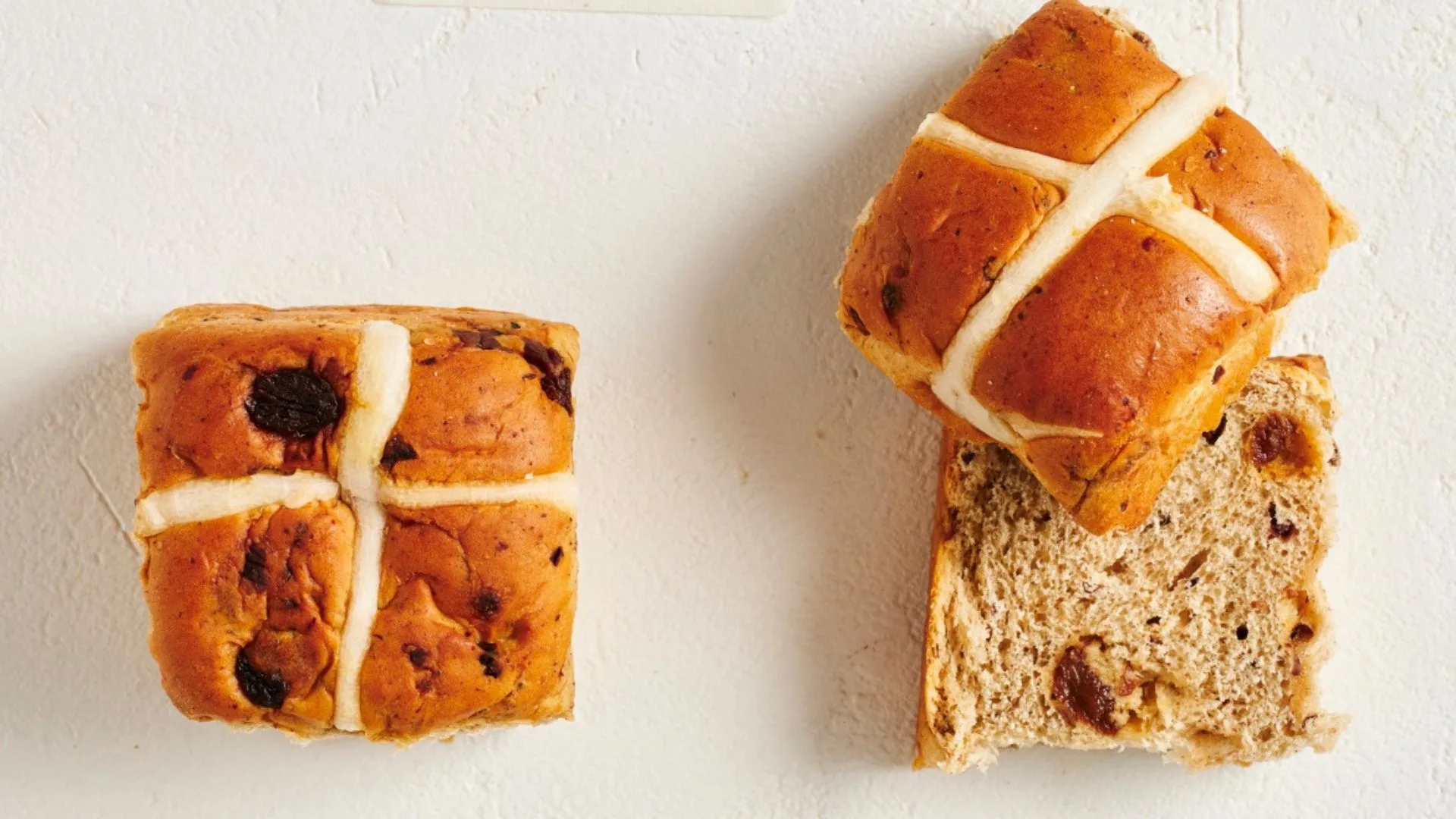 two tradition hot cross buns, one cut in half