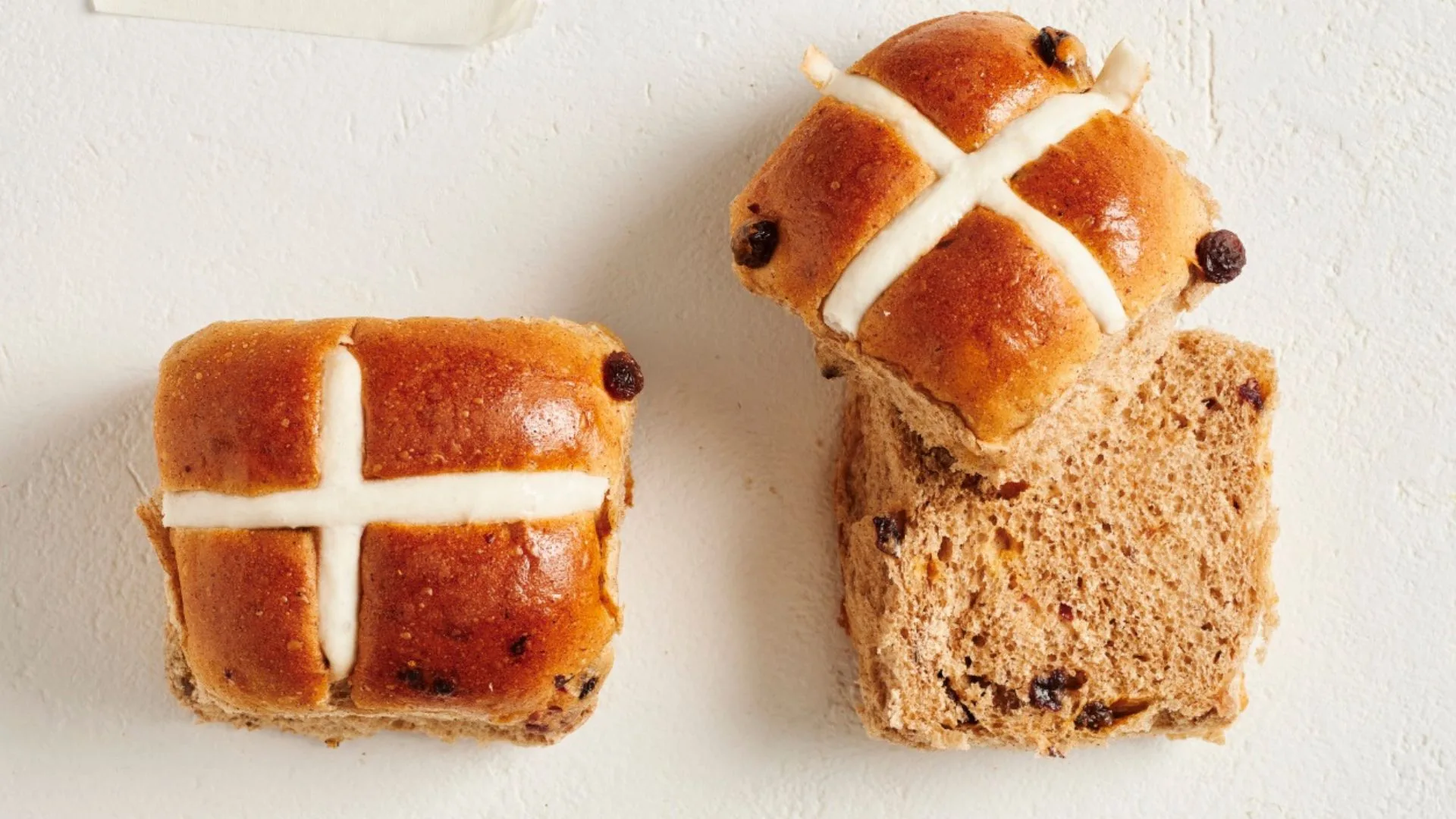 two tradition hot cross buns, one cut in half