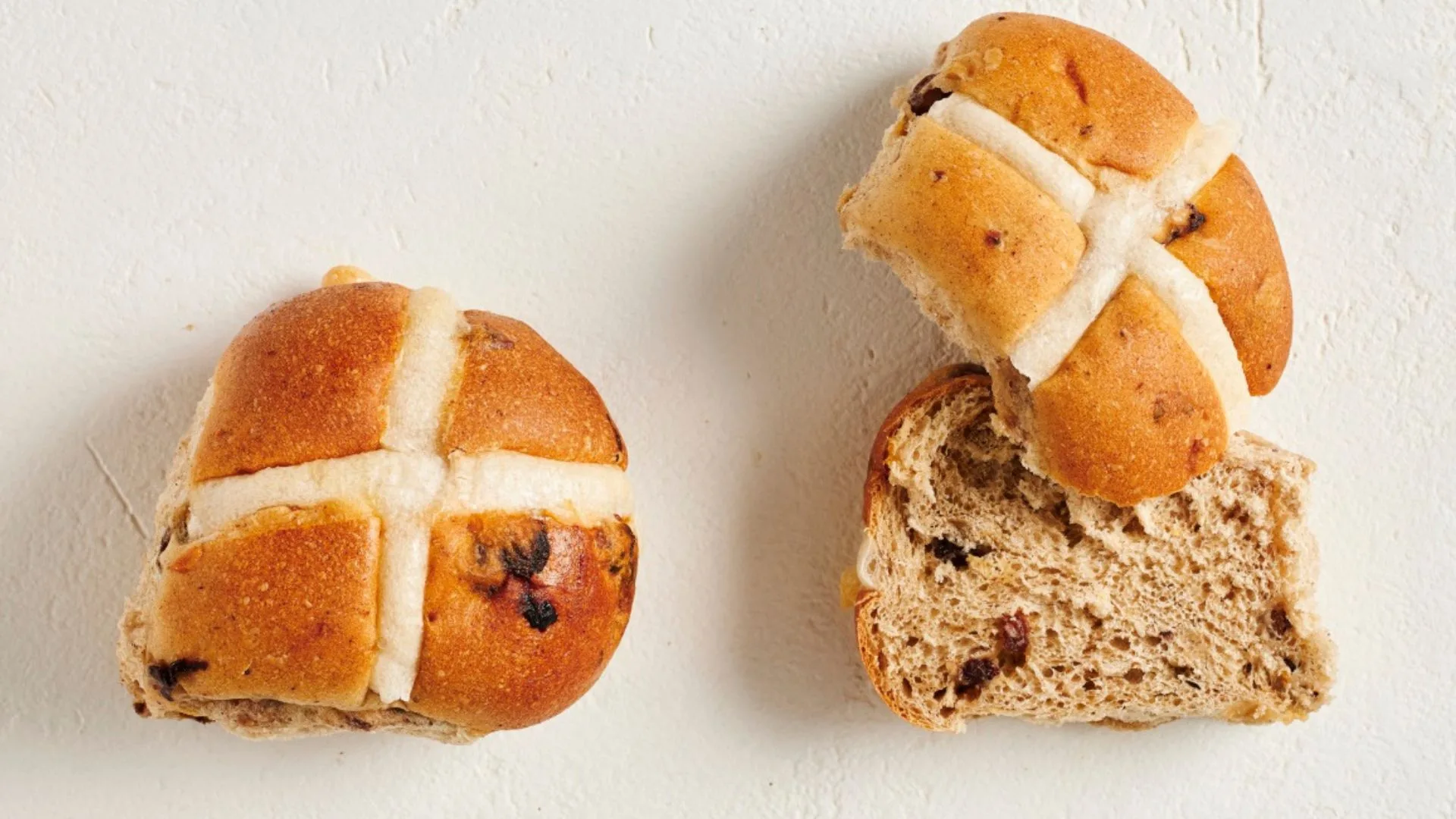 two tradition hot cross buns, one cut in half