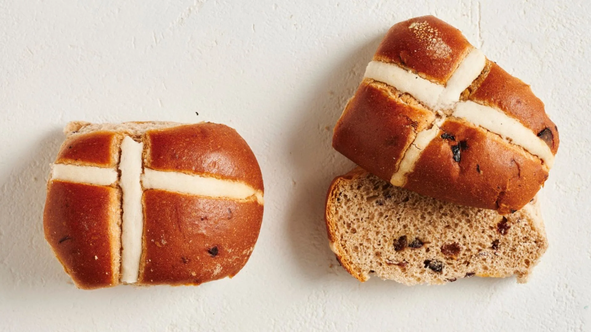 two tradition hot cross buns, one cut in half