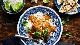 slow cooker chicken recipes butter chicken in a bowl with a blue rim, with small bowls of rice and roti