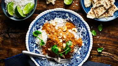 slow cooker chicken recipes butter chicken in a bowl with a blue rim, with small bowls of rice and roti