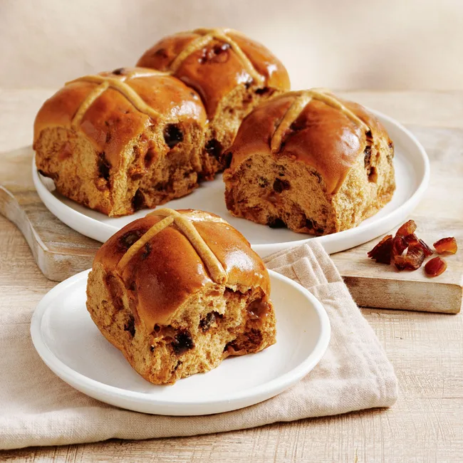 four Sticky Date Inspired Hot Cross Buns by Coles on a chopping board