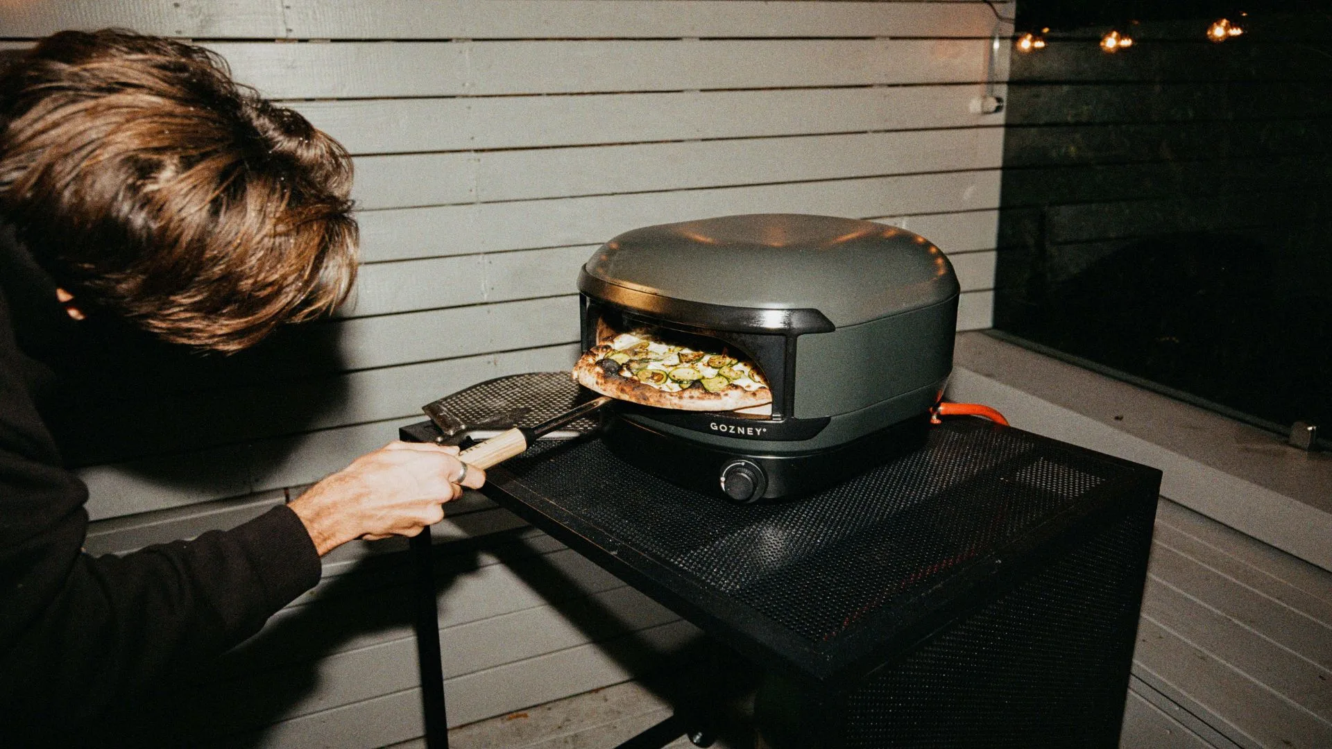 A person sliding a gourmet vegetable pizza into the Gozney Arc Lite oven on a modern outdoor balcony.