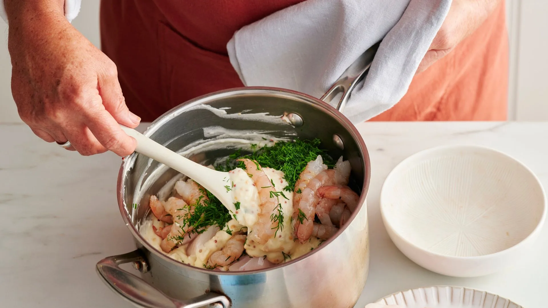 A hand stirs fish pie filling in a saucepan