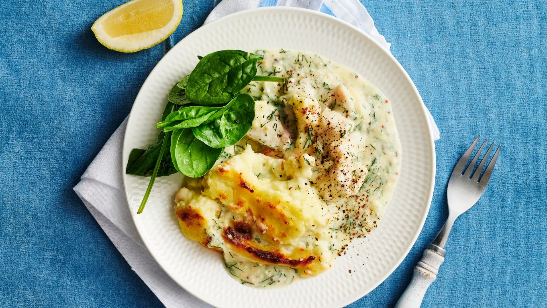 a serving of fish pie on a white plate with a lemon wedge