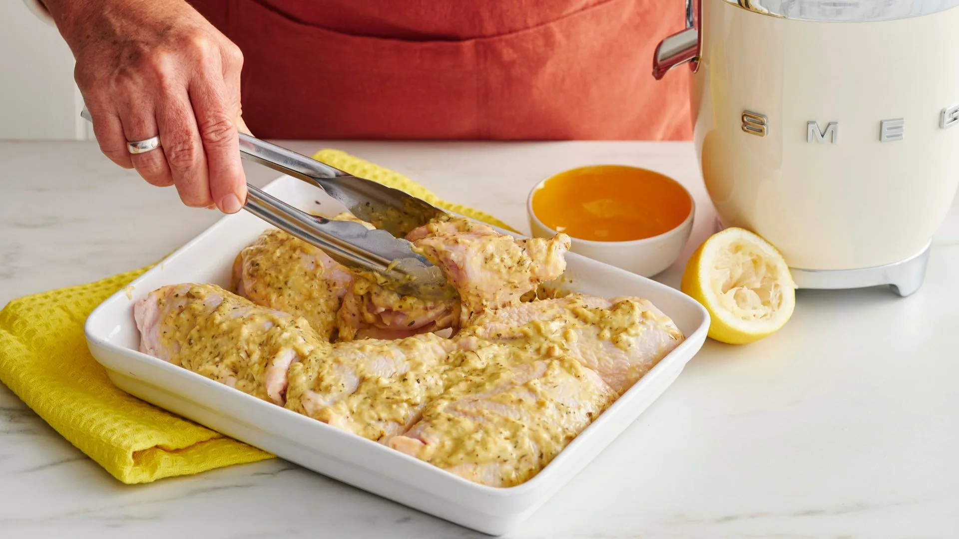 Chicken thighs coated in lemon marinade in a white baking dish