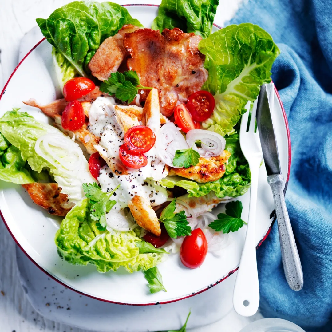 Smoky chicken BLT salad on a white plate with a knife and fork