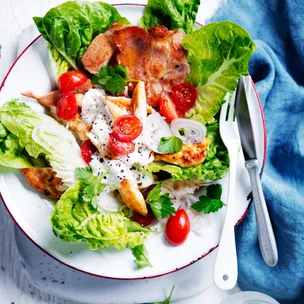 Smoky chicken BLT salad on a white plate with a knife and fork