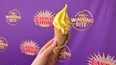 A hand holds an ice-cream cone in front of a purple Sydney Royal Easter Show 2026 banner