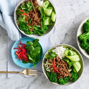 two thai beef rice bowls and a plate of fresh veg
