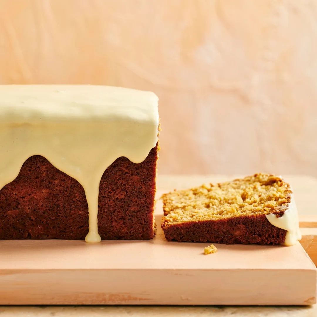 anzac loaf cake with white icing, and one slice cut from the main loaf