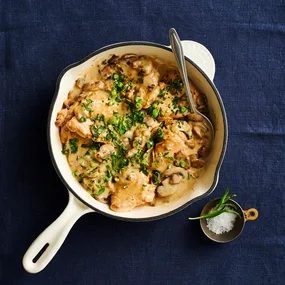 creamy chicken and mushroom in a white frying pan on a dark blue surface