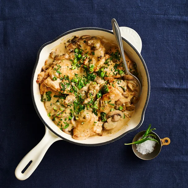creamy chicken and mushroom in a white frying pan on a dark blue surface