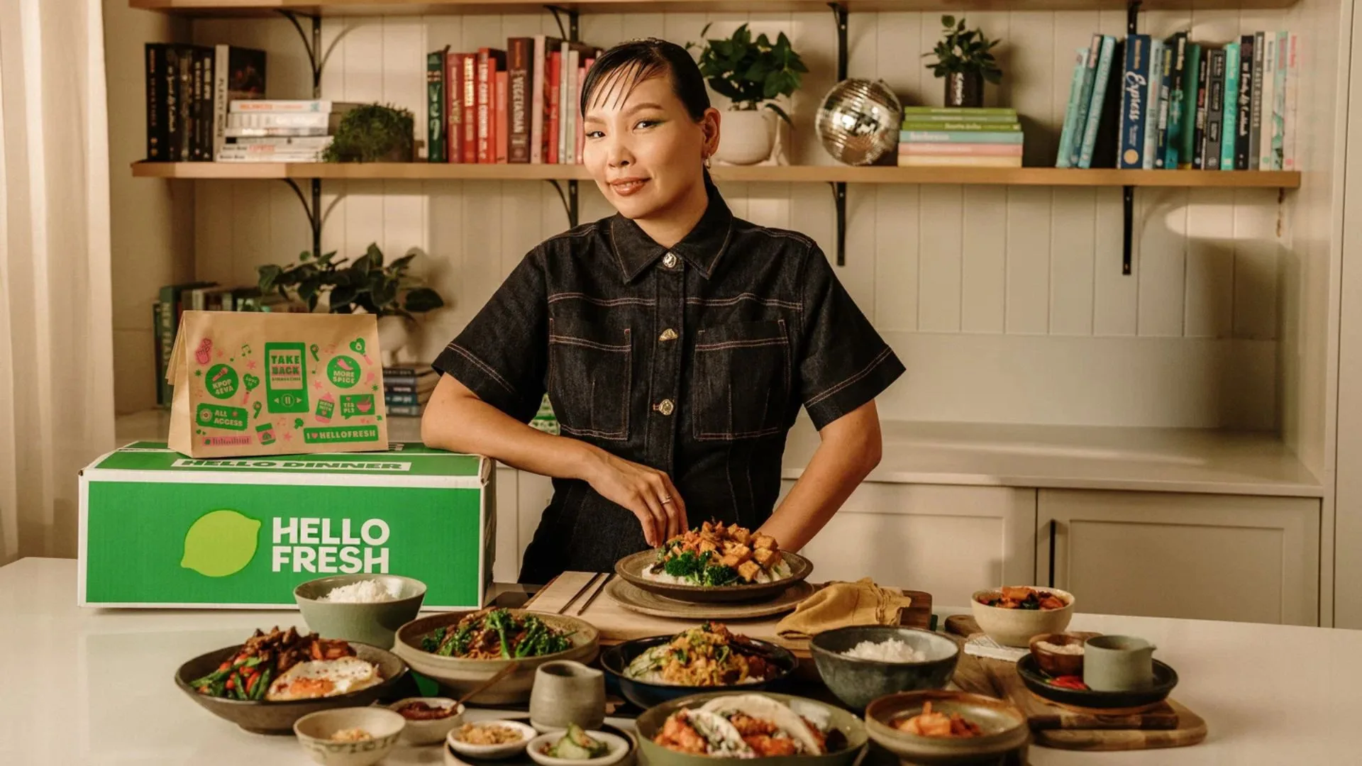 ARIA-winning artist Dami Im posing with the HelloFresh K-Pop Dinner Hunters Box and various prepared meals on a kitchen island. Article - Korean meal kits Australia