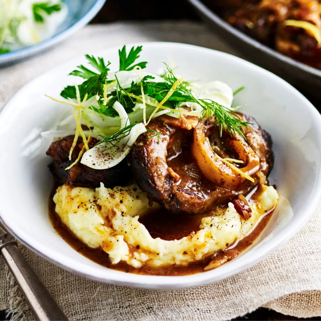 italian slow cooker osso bucco in a white bowl with mashed potato