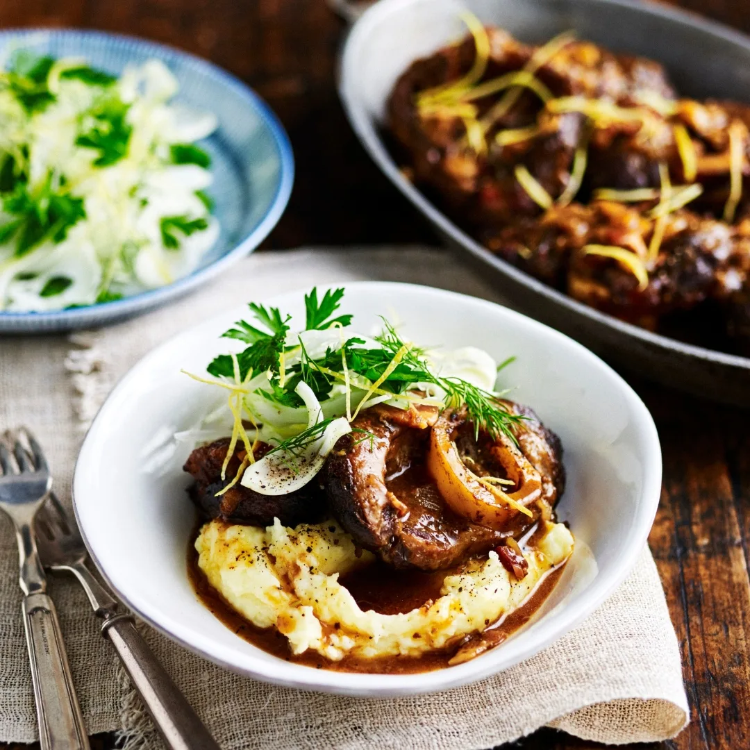 italian slow cooker osso bucco in a white bowl with mashed potato
