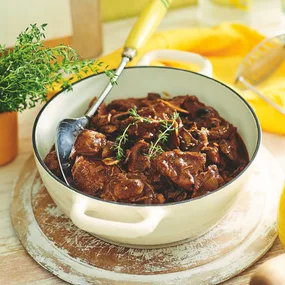 chuck steak and mushroom beef stew in a white serving dish with a large spoon