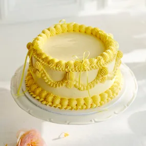 vintage cake with yellow piped icing on a white cake stand