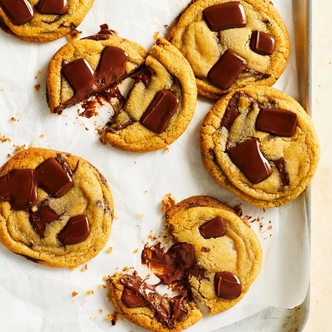 Basic chocolate chip cookies on an oven tray, two are broken in half to show the gooey chocolate