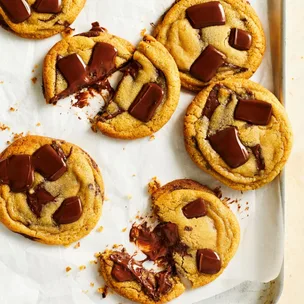 Basic chocolate chip cookies on an oven tray, two are broken in half to show the gooey chocolate