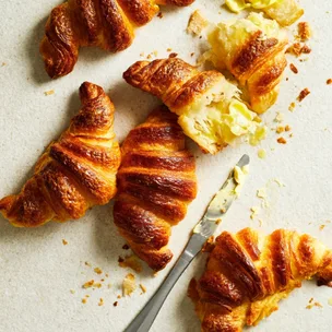 Croissants scattered on a bench with one cut open and buttered.