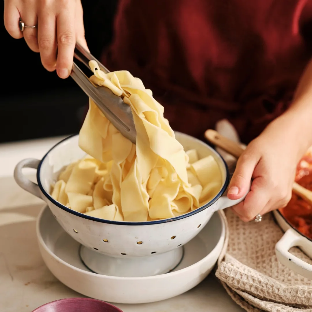 fresh egg pasta dough in a white colander being lifted with tongs