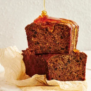 Fruit loaf cut in half, with one stacked on the other, drizzled with honey
