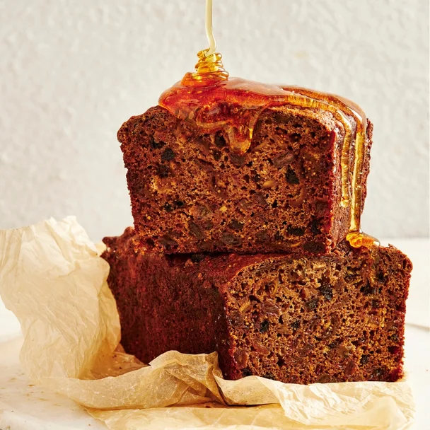Fruit loaf cut in half, with one stacked on the other, drizzled with honey