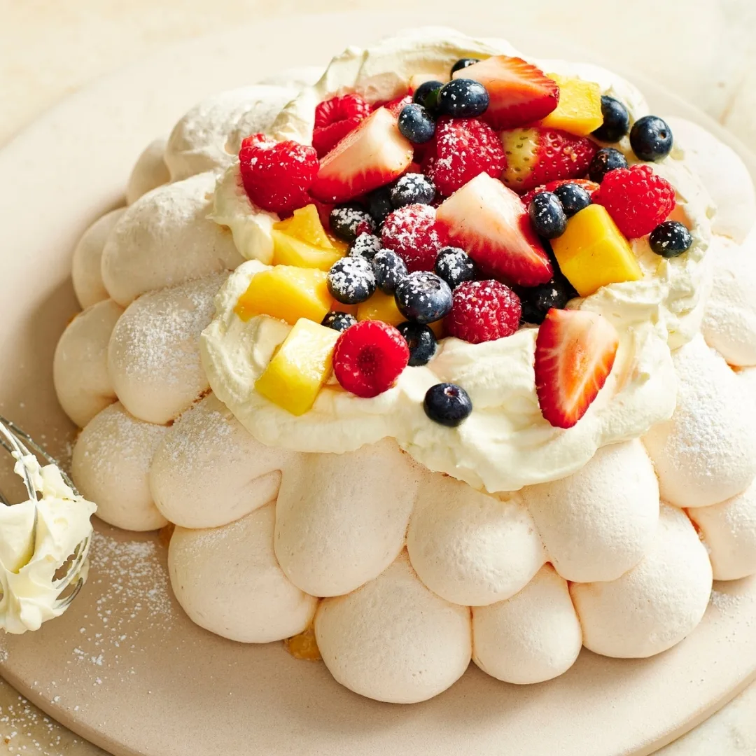 Decorative pavlova topped with berries and mango pieces and dusted with icing sugar