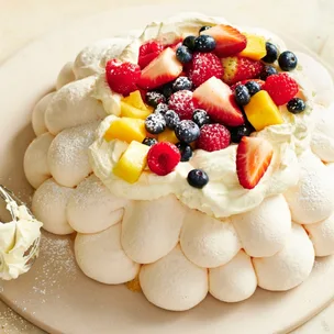 Decorative pavlova topped with berries and mango pieces and dusted with icing sugar