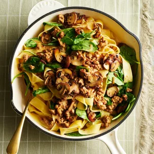 pork mince pasta with spinach and mushroom in a white frying pan with a spoon