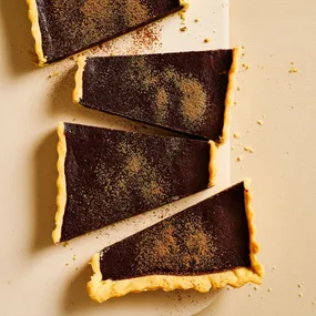 Rich chocolate tart, cut into four big pieces diagonally and dusted with cocoa powder.