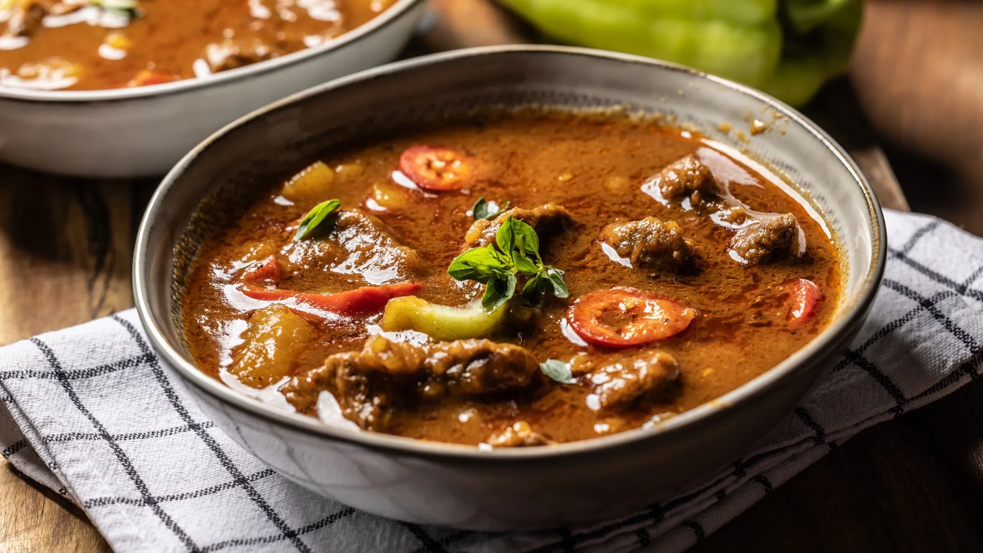 A hearty bowl of Hungarian goulash soup featuring tender beef, potatoes, and red sweet peppers in a rich, paprika-infused broth, garnished with fresh herbs.